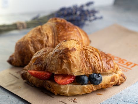 A crisp croissant filled with fresh strawberries and blueberries on a rustic background.