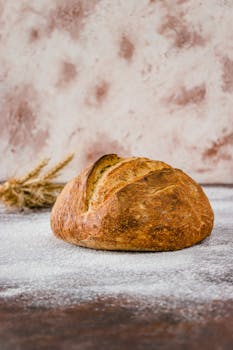 Freshly baked rustic whole wheat bread with flour-dusted surface in a warm kitchen setting.